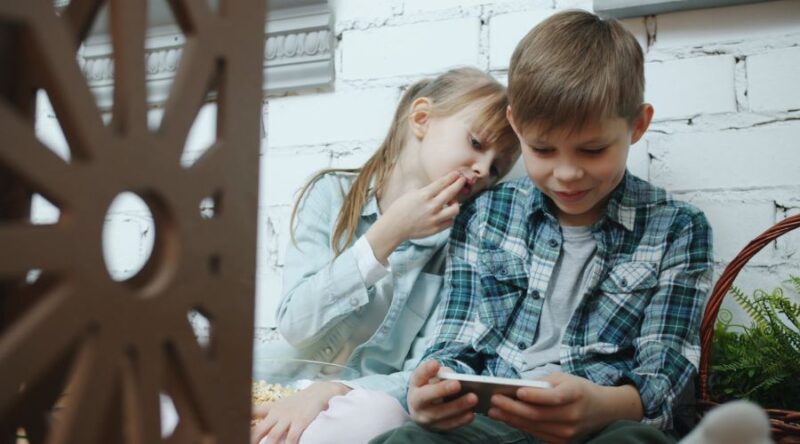Dečak i devojčica sede i gledaju sadržaj na pametnom telefonu.