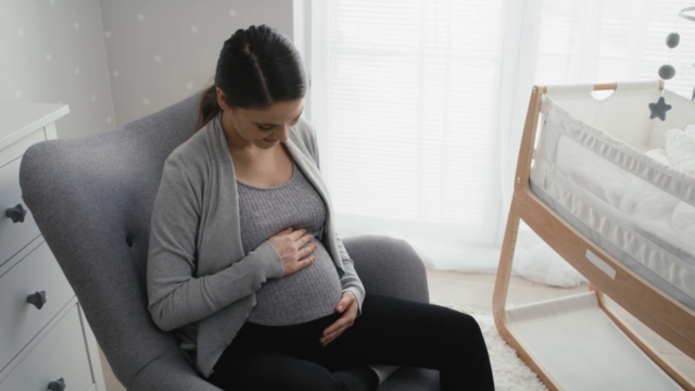 Trudnica sedi u fotelji pored kreveca držeći se za stomak