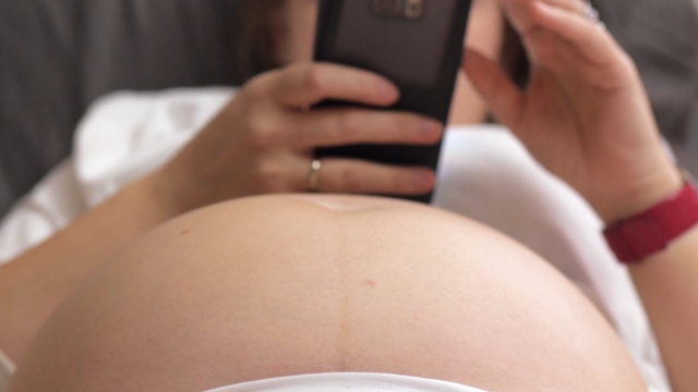 Trudnica leži u krevetu i koristi telefon